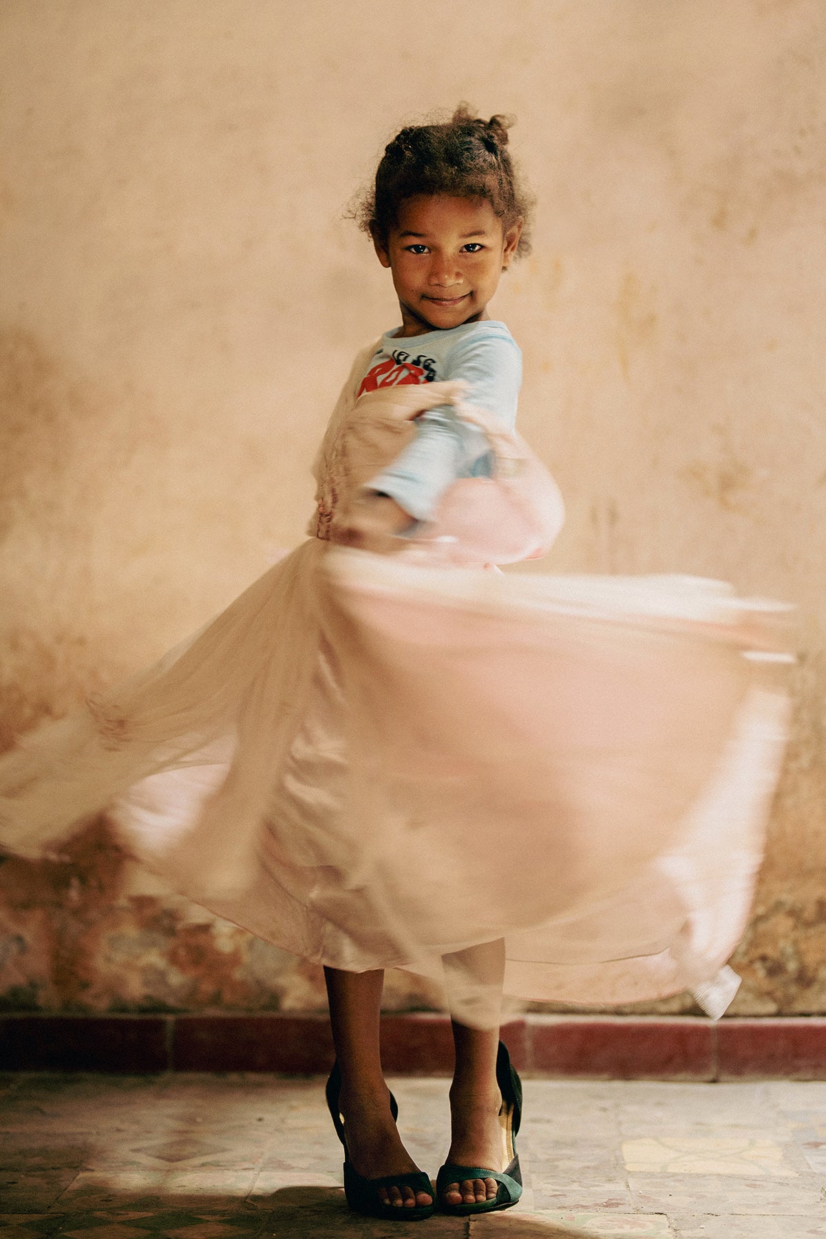 Art print of a young girl in a light blue top and pink skirt twirling in front of a textured wall.