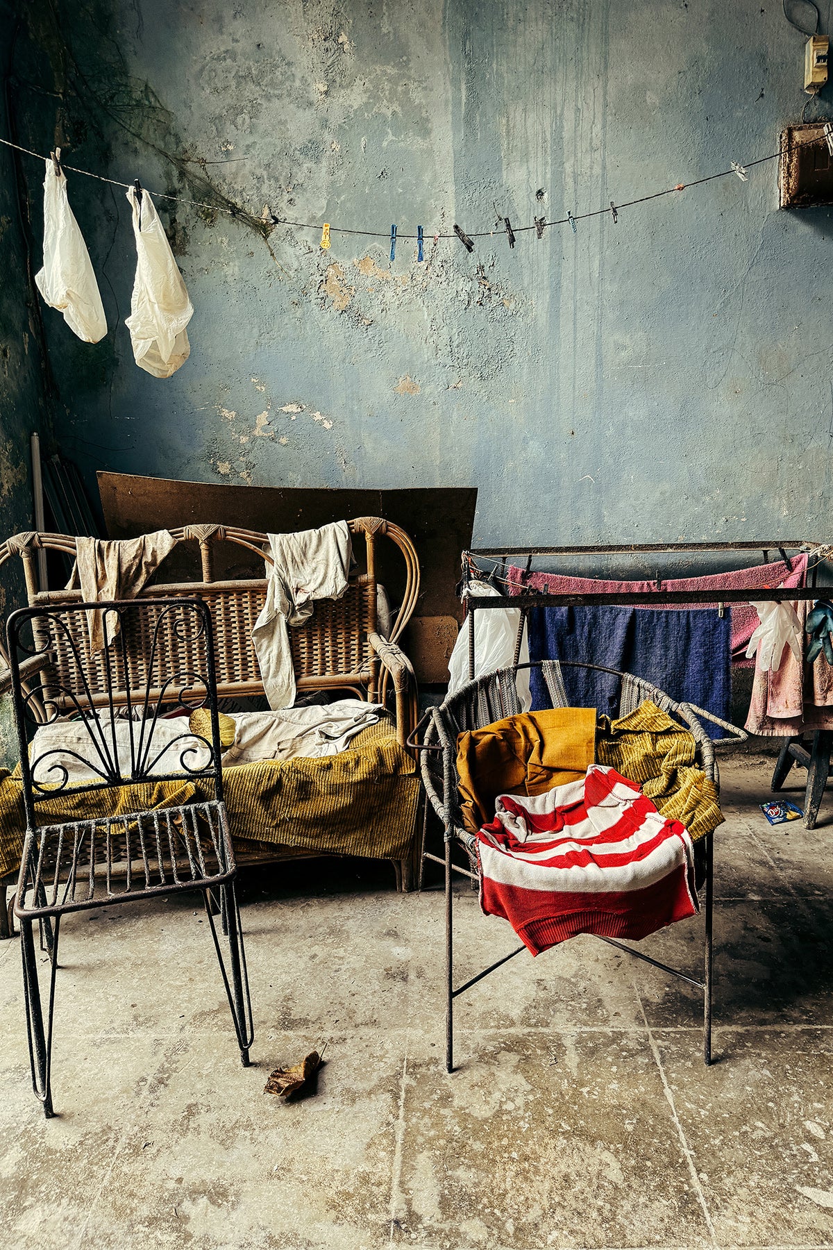 Cuban room with wicker chair, metal chair, and clothes hanging on a line against a textured wall.