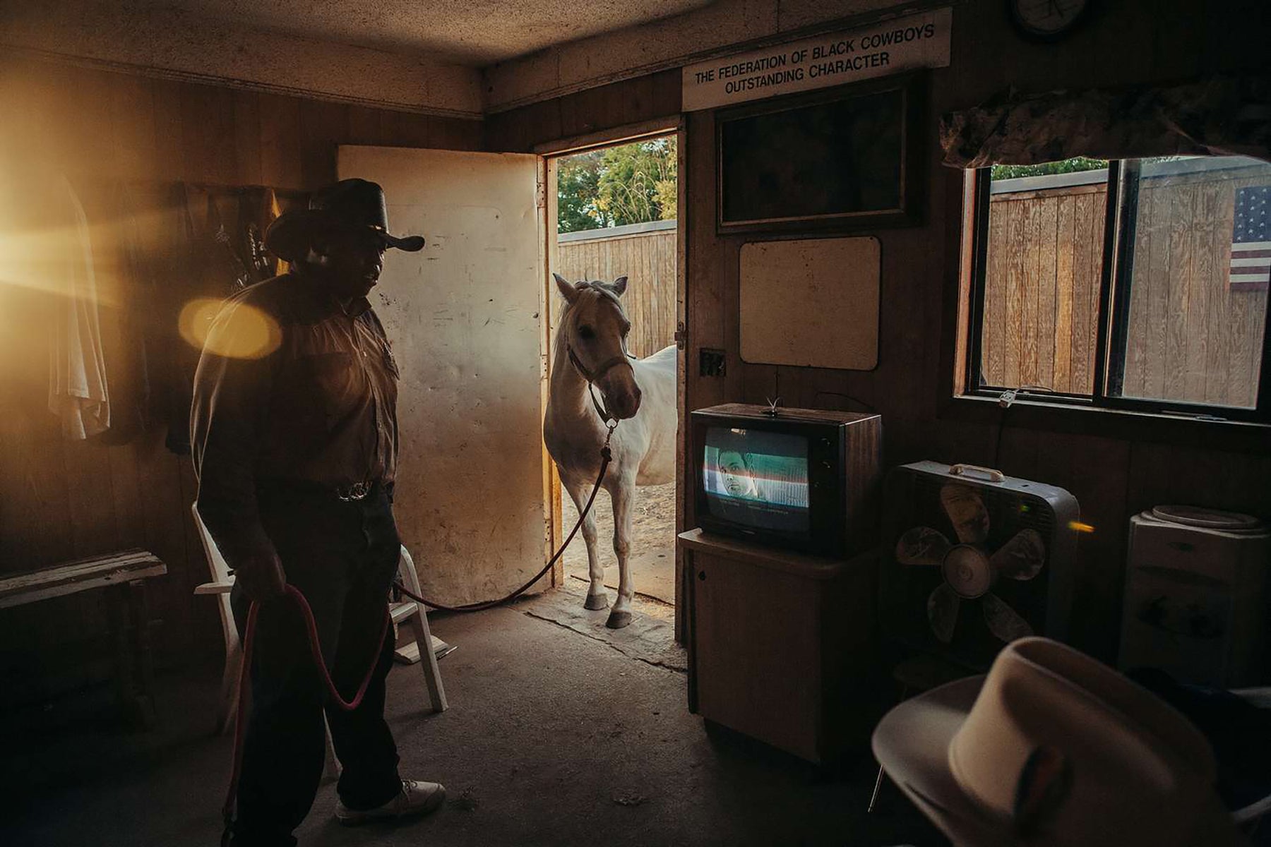Fine art print of a black cowboy leading a horse through the open door of his living room on a sunny day.