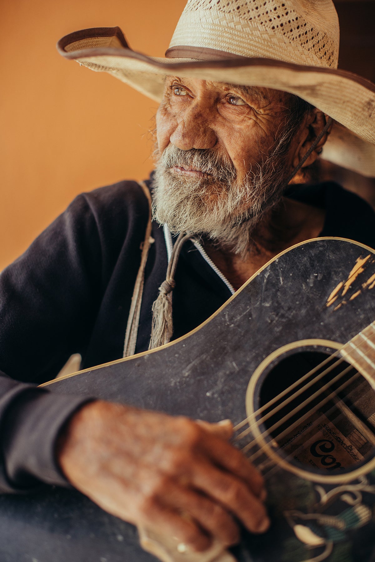 Man wearing a straw hat holding an acoustic guitar against a warm-toned background