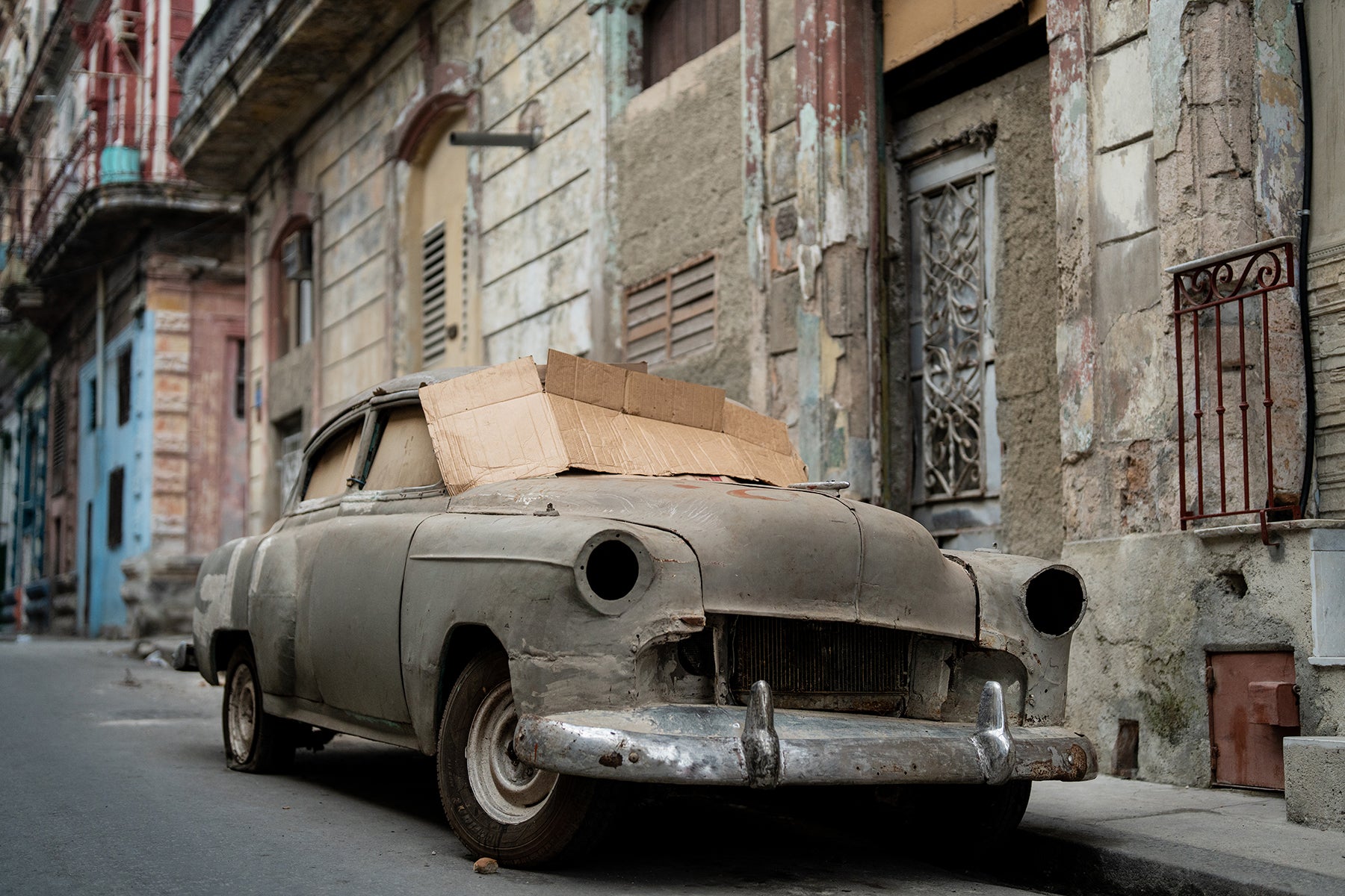 Fine art color print of an abandoned old car with cardboard windows on the streets of Cuba.