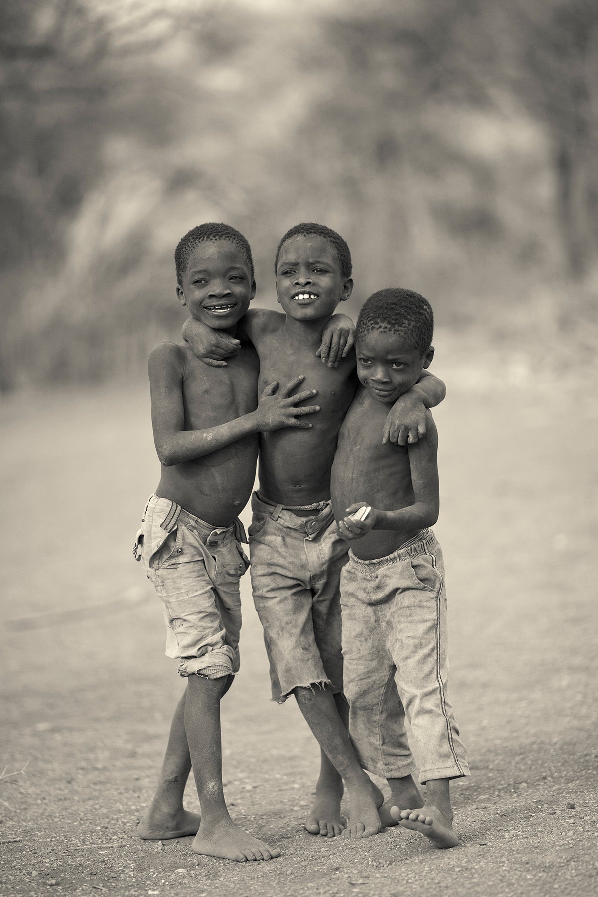 Three young Hadza boys standing together outdoors in a natural setting.