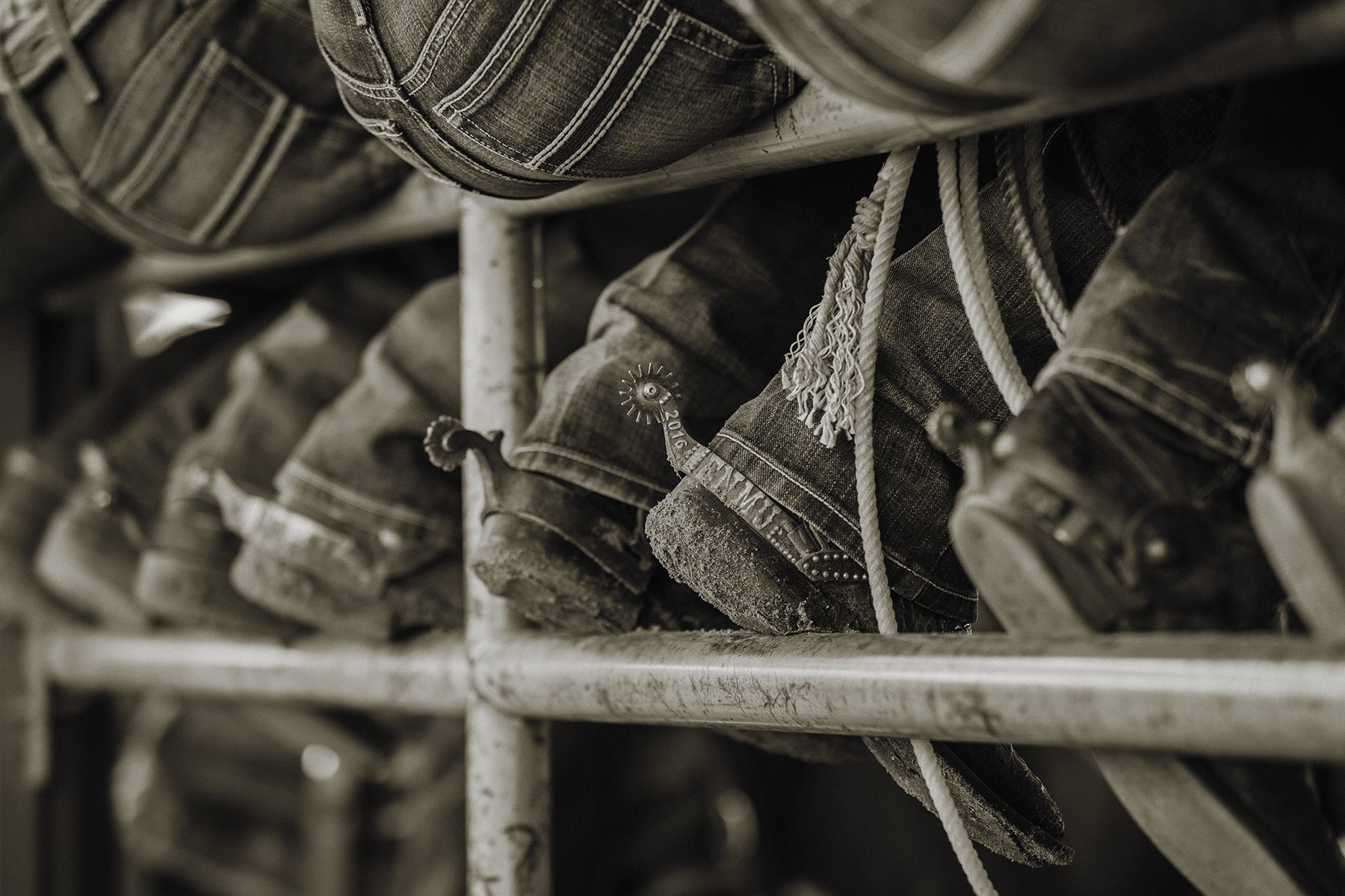 Close-up of cowboy boots with spurs from multiple cowboys resting on an iron gate as they sit on top.