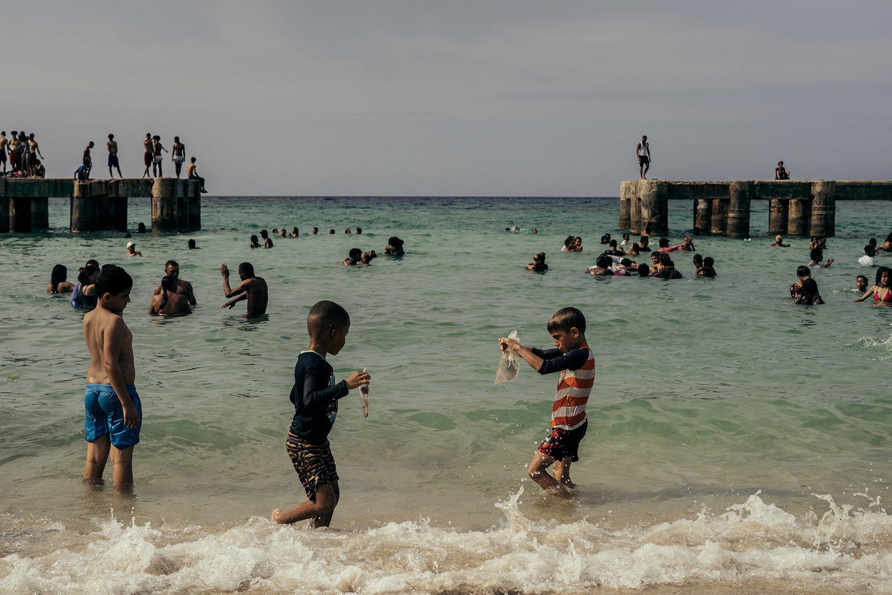 Art print of children playing in the water at a beach with a pier in the background in Cuba