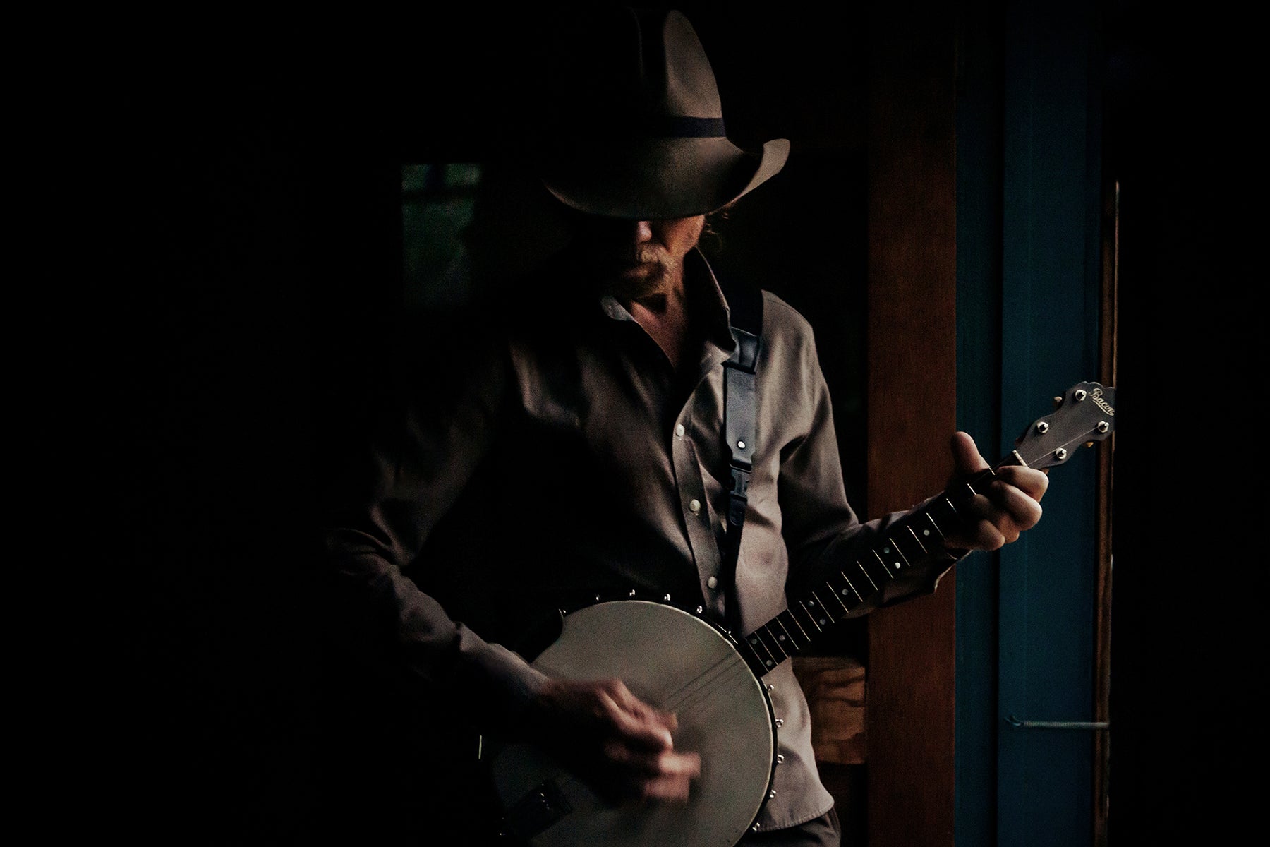 Color art print of a banjo player in a cowboy hat with his eyes tucked behind the brim.