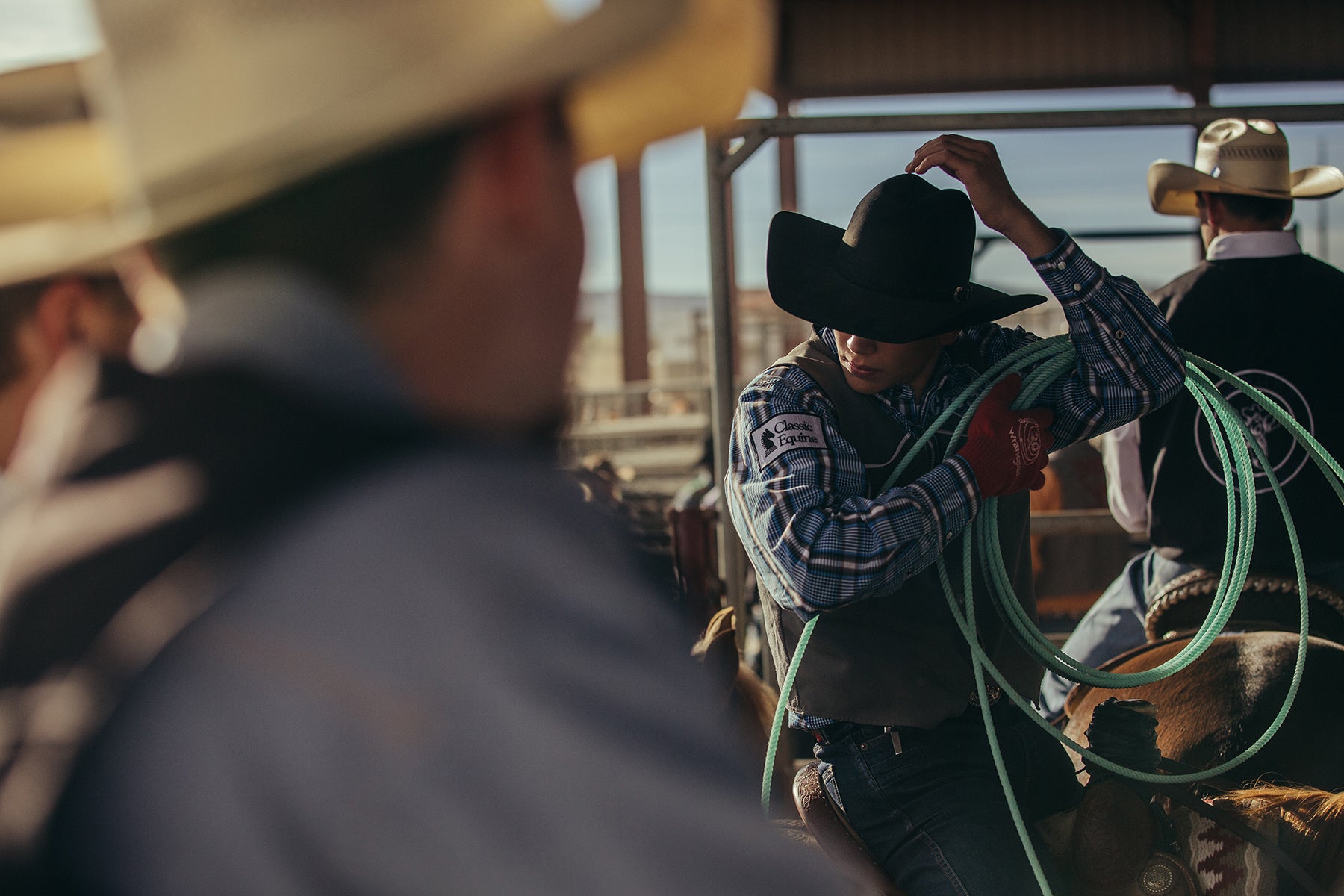 Fine art color print of cowboys in a rodeo arena with one adjusting a lasso.